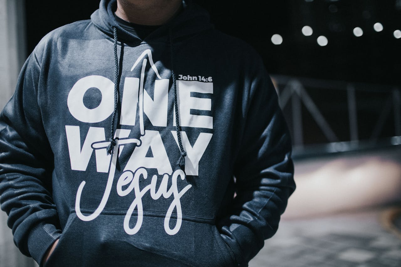 Close-up of a man in a hoodie with 'One Way Jesus' text on a dark street.